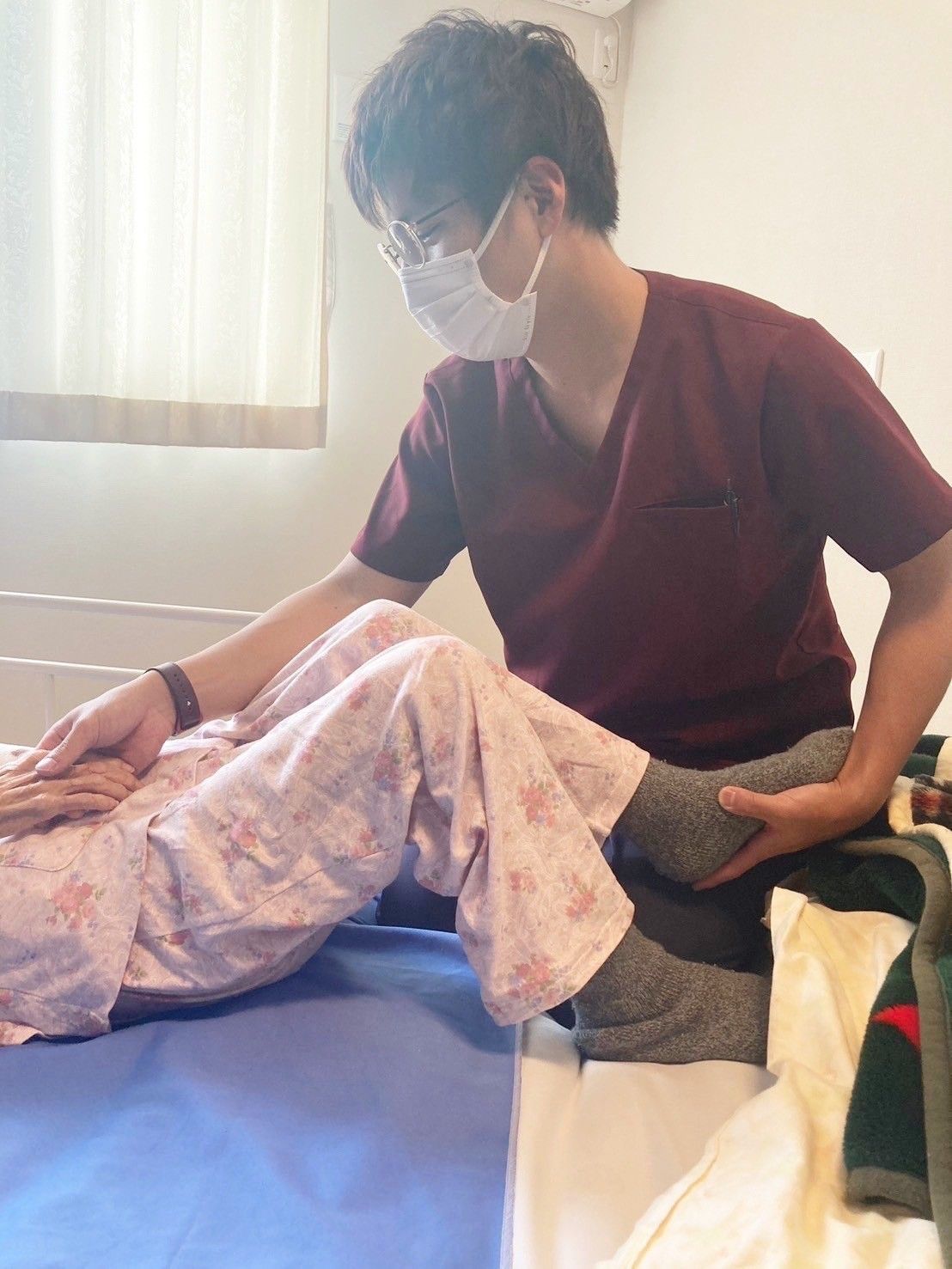 緑の多い屋外で笑顔で過ごしている車いすの高齢女性とエプロンを付けた女性スタッフ。