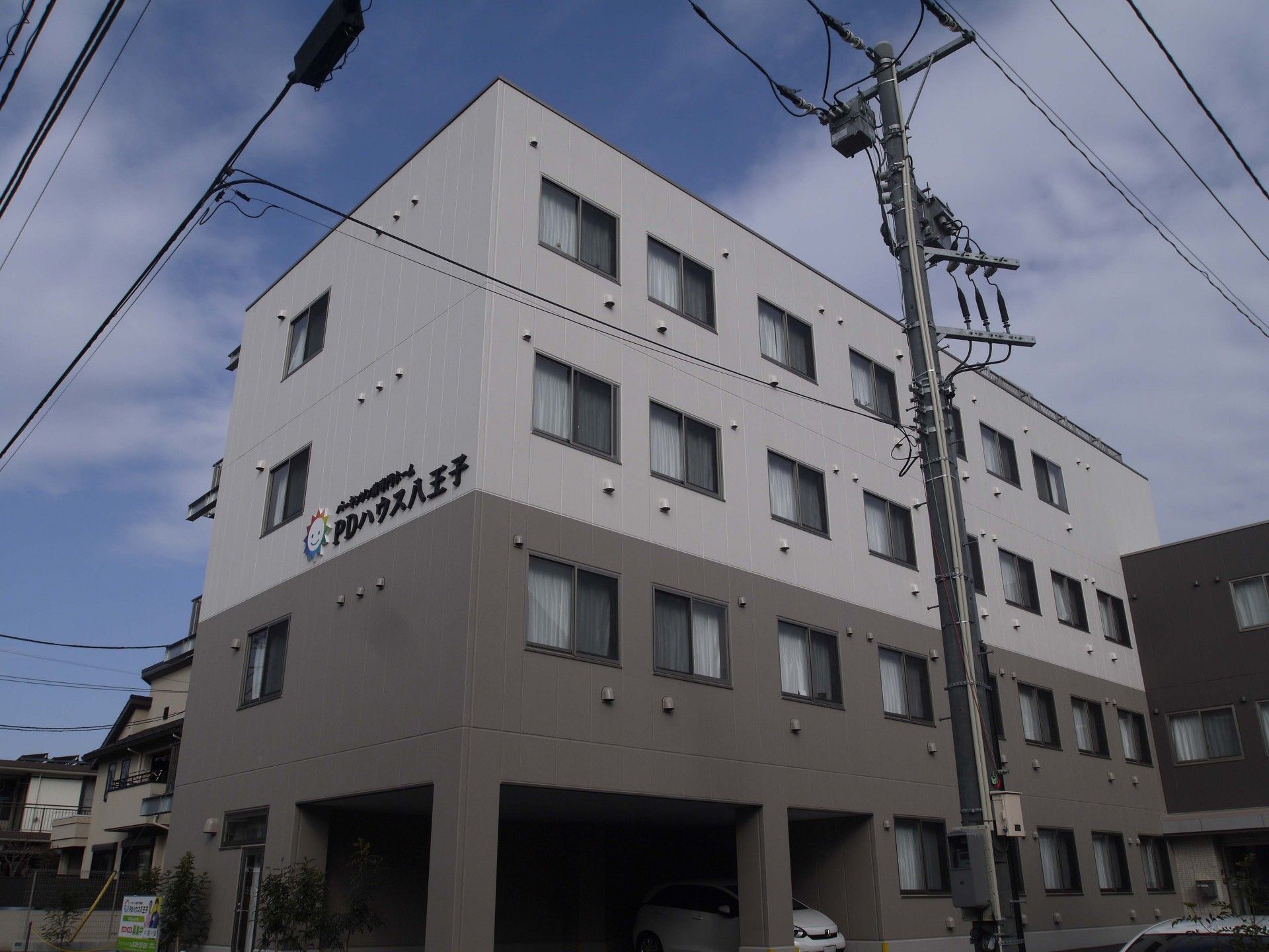 4階建ての建物はブラウン系の外壁で、1階部分には駐車場があり、車が数台止まっている。