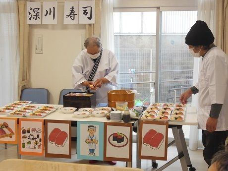テーブルの上にはたくさんの寿司が並べられていて、マスクをした職人が寿司を握っている。