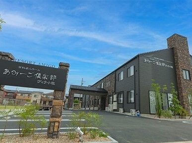 広い駐車場が付いた２階建ての建物は日当たりのいい場所に建っている。ダークグレーの外壁で車寄せもある。