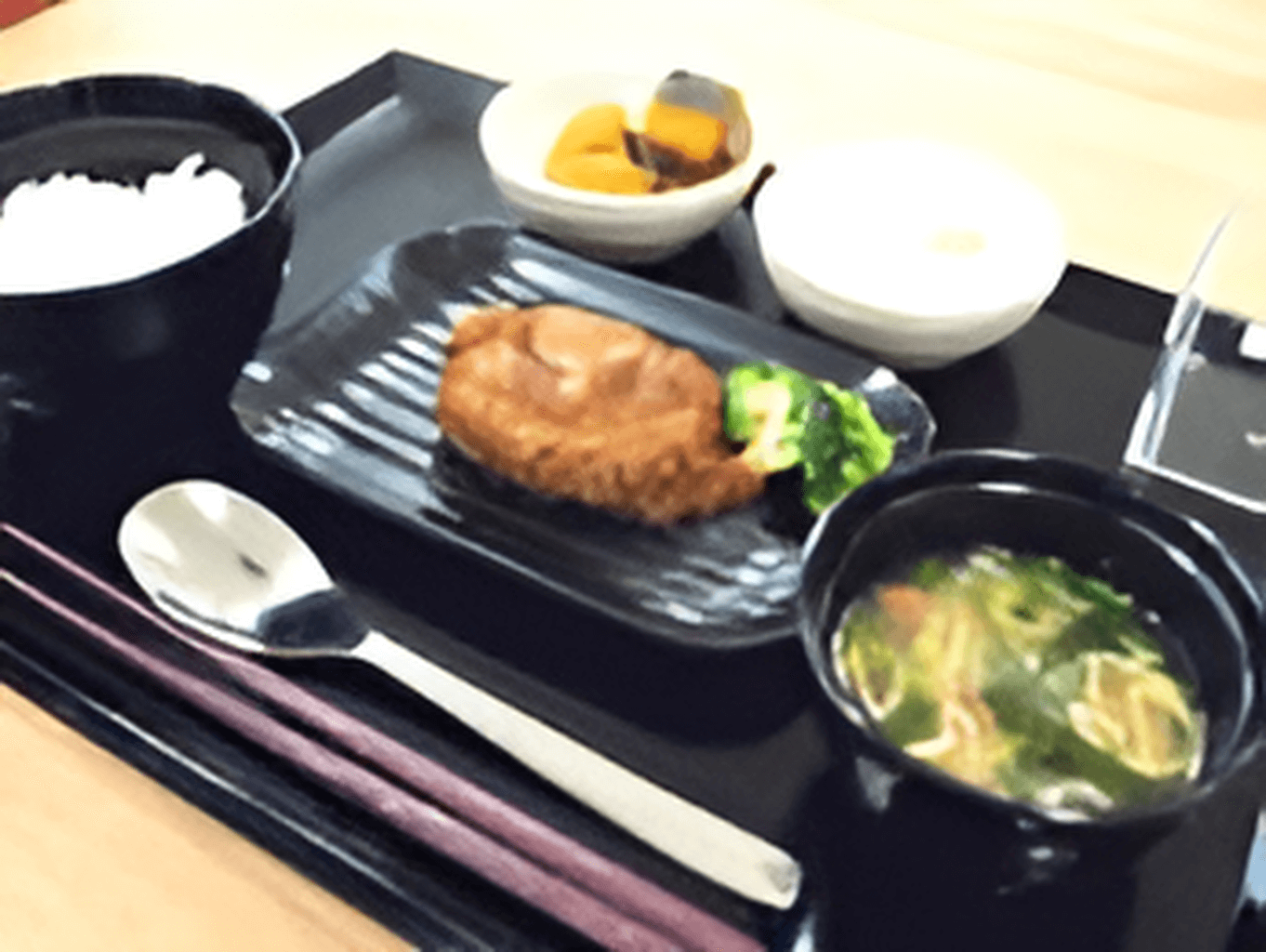 黒いトレーに白いご飯やみそ汁、メンチカツ、かぼちゃの煮物などが並んでいる。