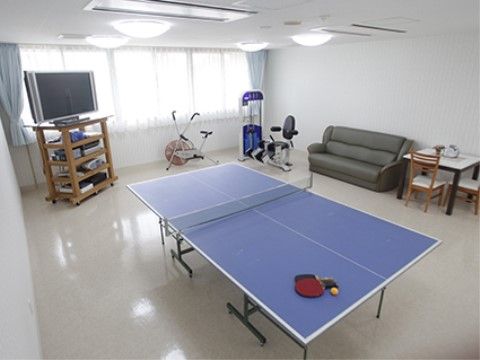 娯楽室にはテレビ、機能訓練用の器具、ソファーが設置されている。部屋の中央には青い卓球台があり、ラケットと球が置かれている。