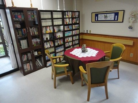 大きな本棚の上には突っ張り棒が付けられており、倒れないようにされている。テーブルの周りには3脚の椅子が置かれている。