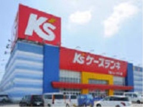 赤、白、黄色、青でデザインされた大きな建物の家電店がある。駐車場は広々としており、多くの車が止められている。