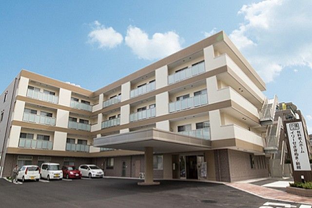 駐車場に車が3台停まっている、ベージュと白の外壁の4階建て有料老人ホーム