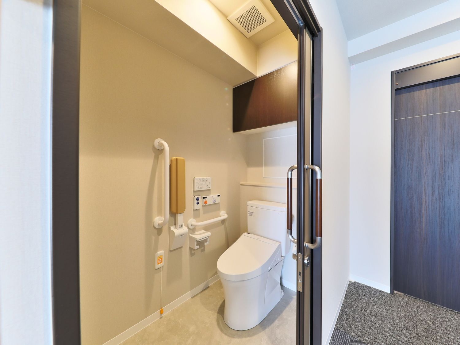 手すりとオレンジの呼び出しボタンが付いたトイレにはスライド式のドアが設置されている。