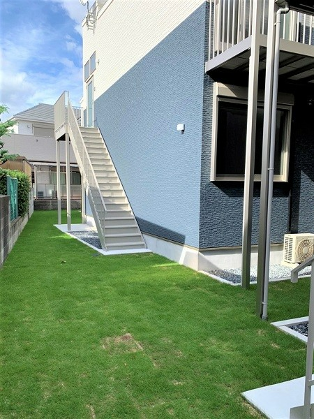 白とダークグレーの外壁の２階建ての建物は横に長く、屋外階段も設置されている。