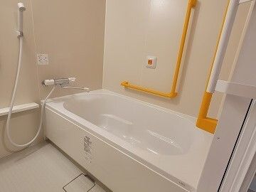 オレンジの呼び出しボタンや手すりが設置された一人用の浴槽がある浴室。