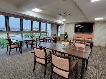 ピンクの椅子がセットされた4人掛けのダイニングテーブルセットが複数置かれた食堂にはテレビもある。