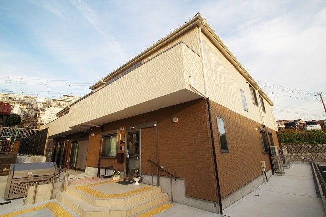 ２階建ての建物は日当たり良好で玄関先には手すり付きのスロープと階段が付いている。