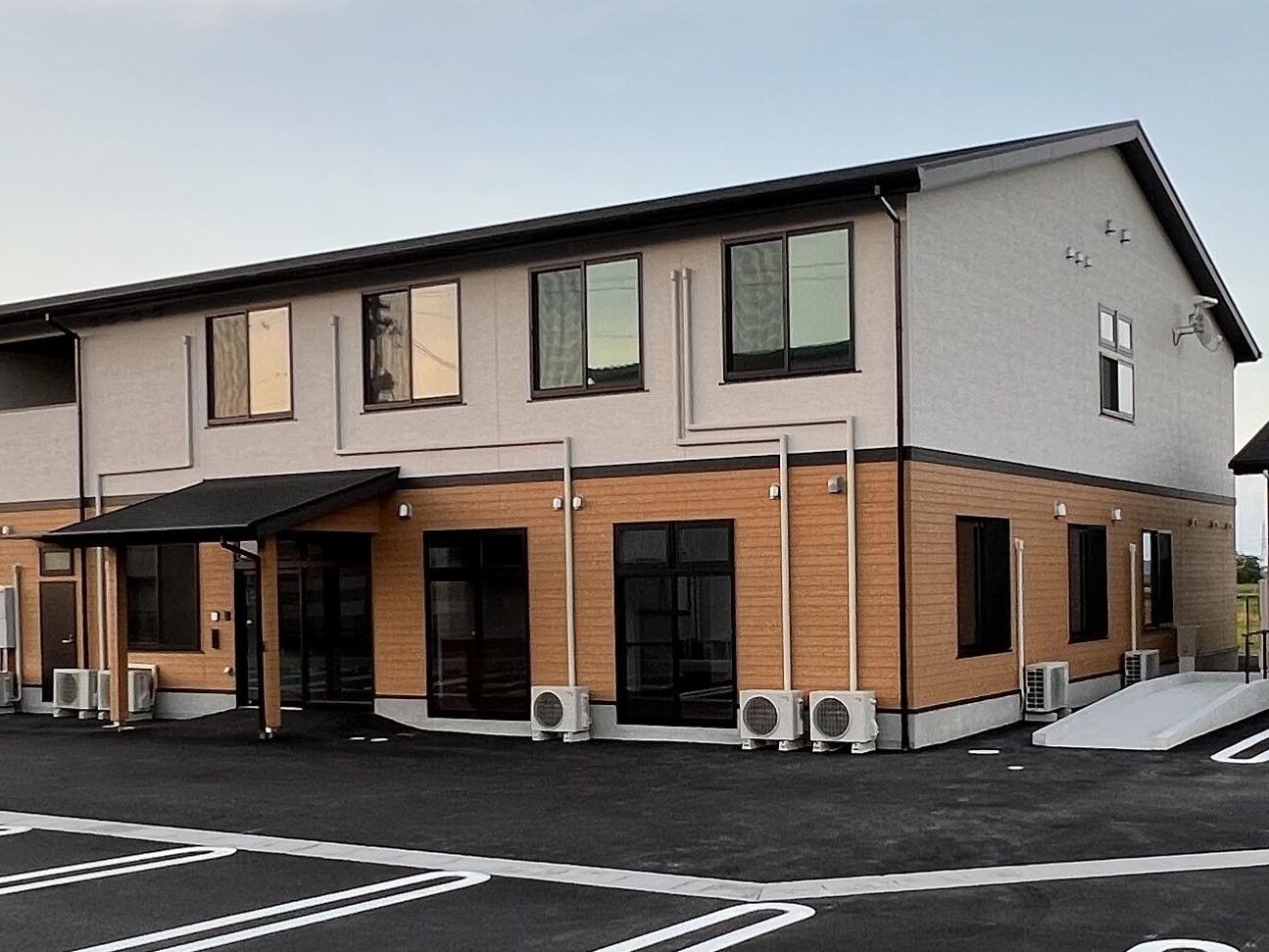 2階建ての建物の玄関部分には屋根があり、窓もたくさんついている。フロアにより外壁の色が異なる。