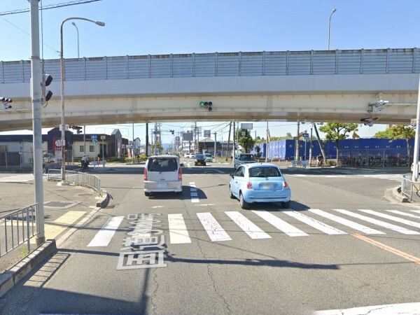 横断歩道のある２車線の道路。前には数台の車が走っていて、奥には草木が植えられた場所がある。