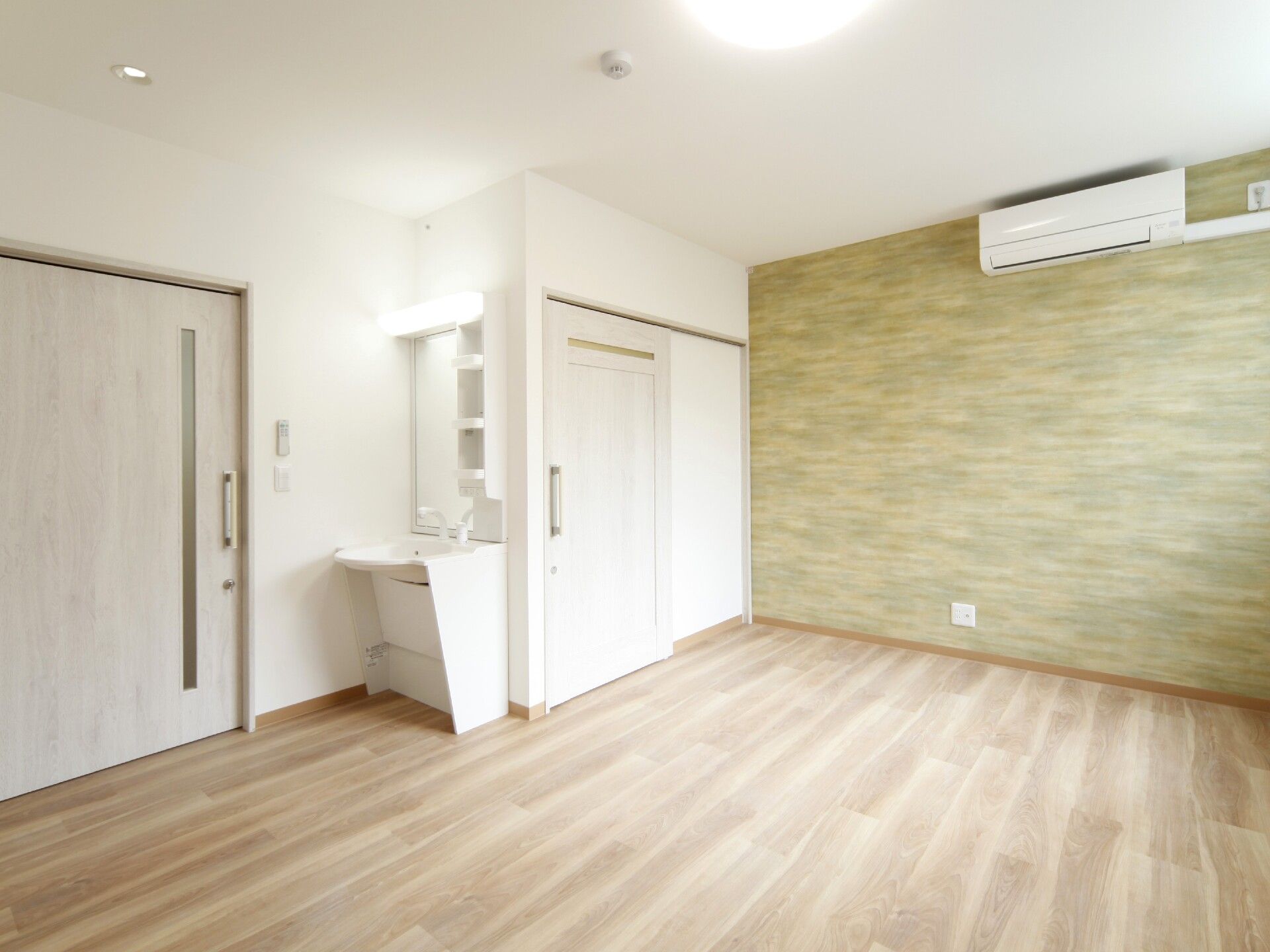エアコンが付いたフローリングの部屋には洗面所やトイレがあり、グリーン系のアクセントクロスもある。
