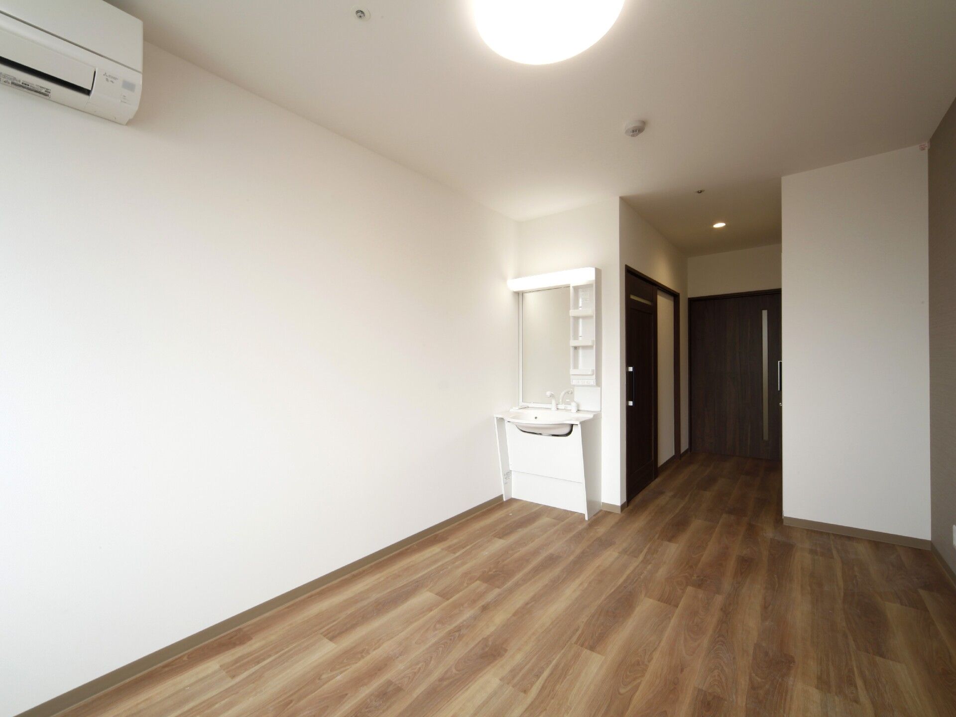 収納棚や鏡が付いた洗面所が部屋の角にあり、壁にはエアコンも設置されている。