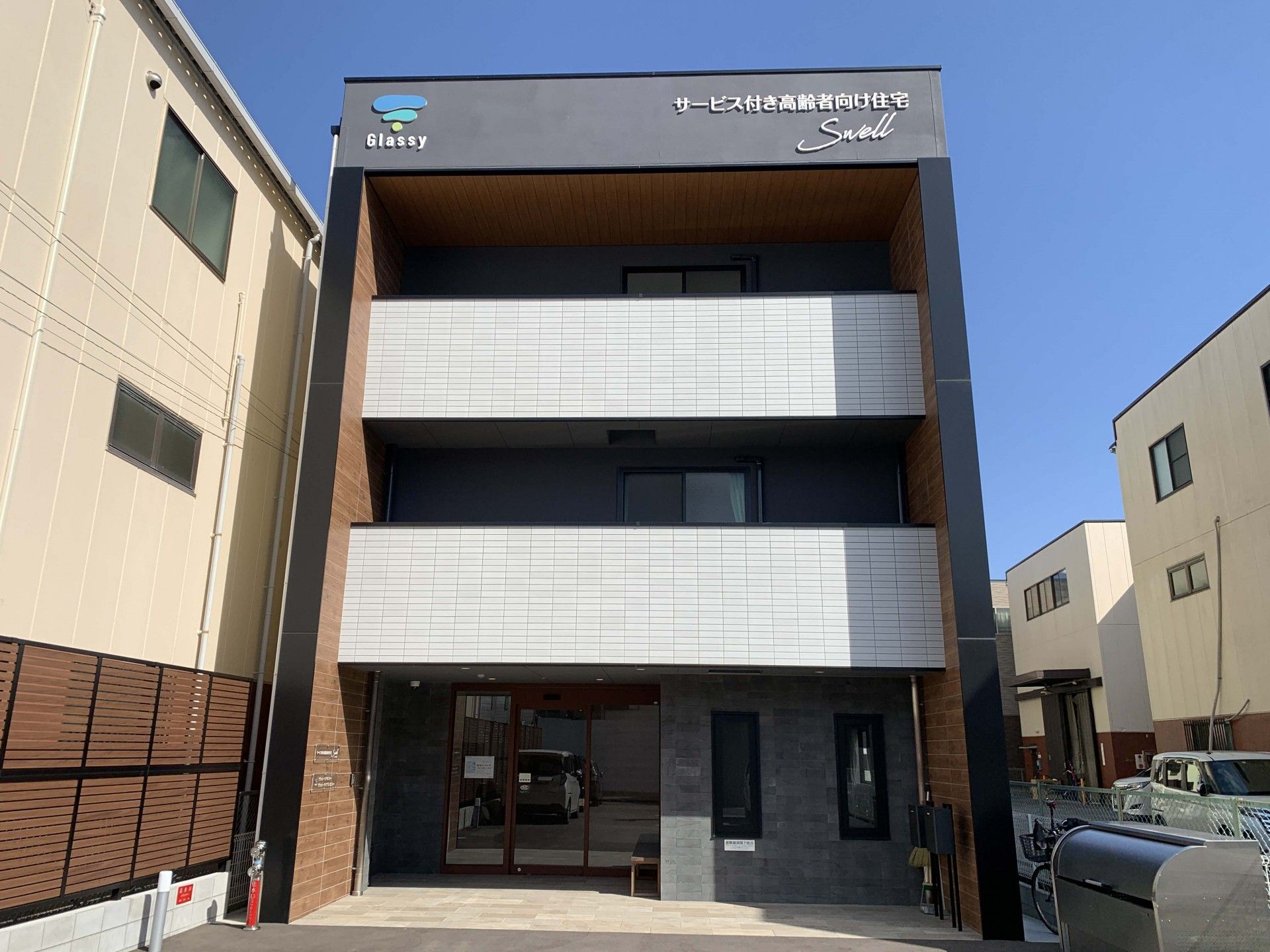 白を基調とし建物は街中に建っていて、各フロアにベランダがあり、外壁に住宅名が書かれている。