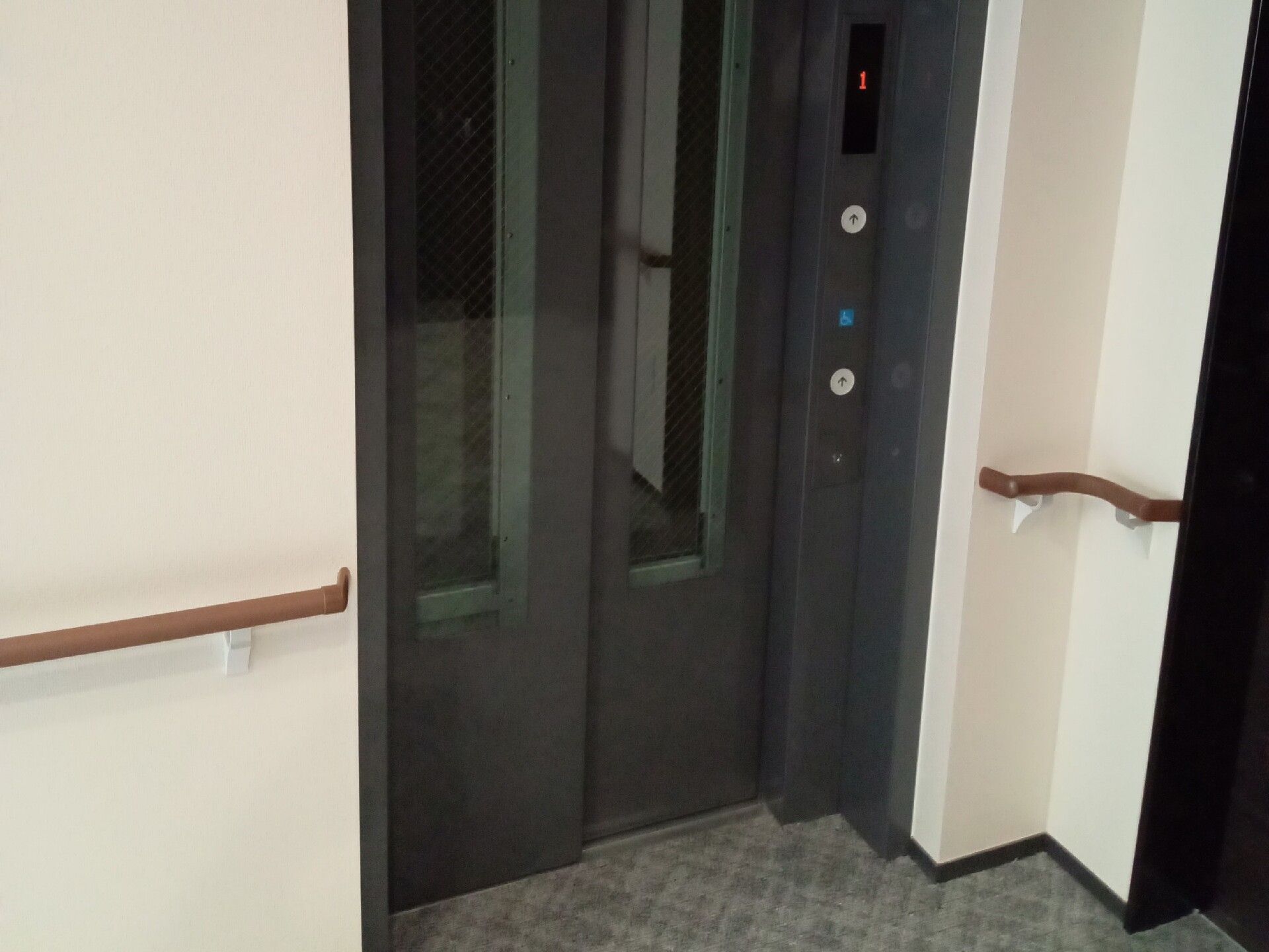 グレーのカーペットが敷かれた廊下の一角にはエレベーターが設置され、壁には手すりが付いている。