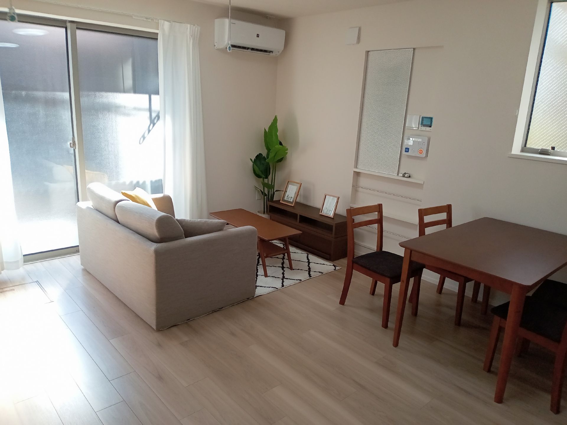 ダイニングテーブルセットやソファが置かれた部屋は明るい雰囲気。エアコンや見守りコントローラーがある。