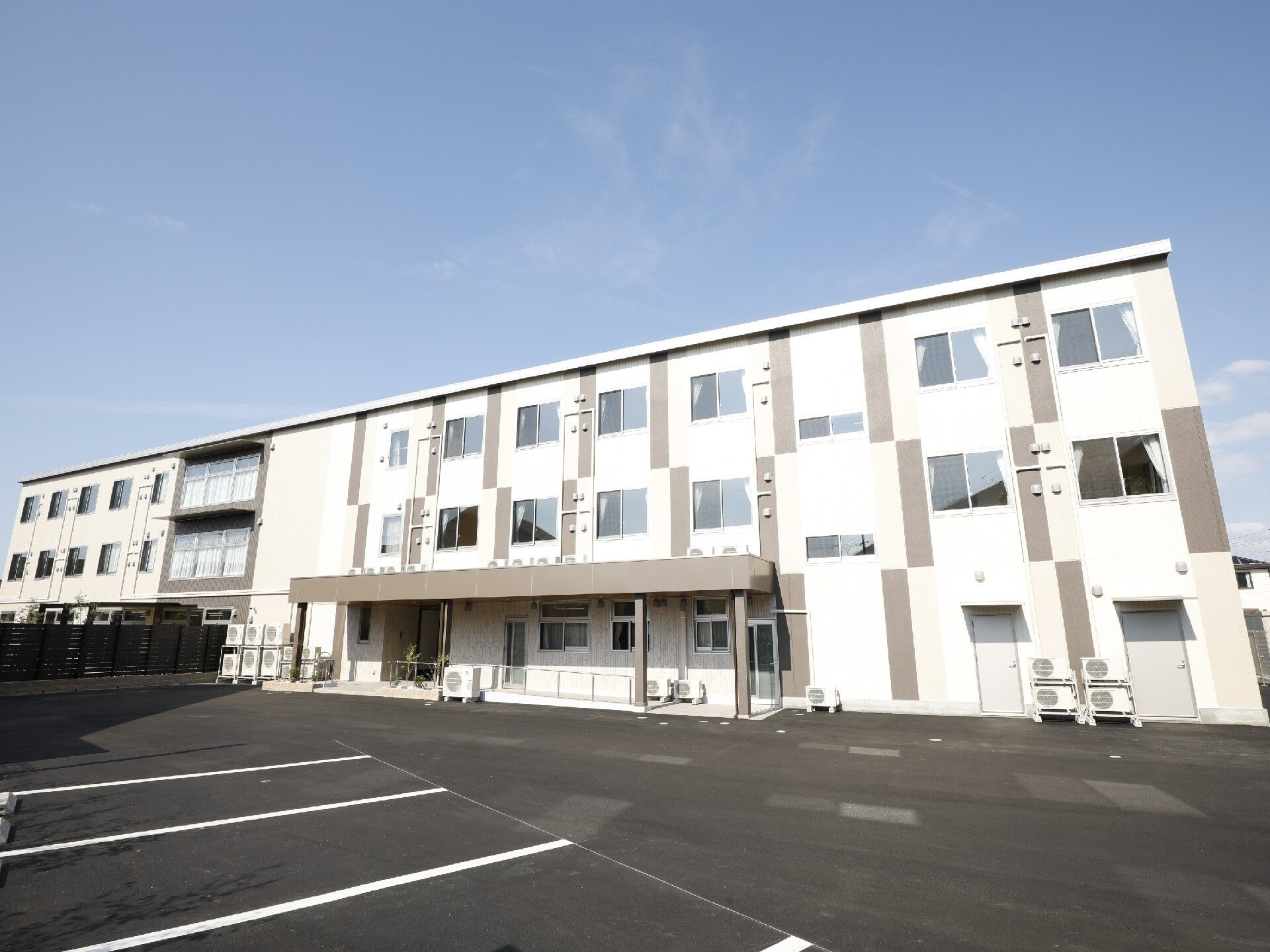 白線が敷かれた広い駐車場があり、白を基調とした３階建ての建物は日当たりのいい場所に建っている。