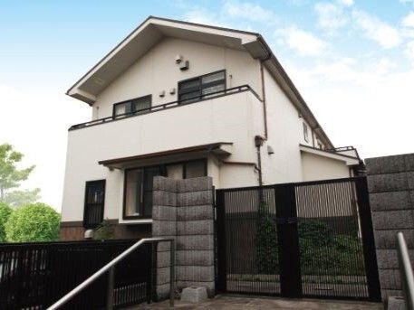 三角屋根の２階建ての建物は白い外壁で2階部分にはベランダが付き、門が閉まっている。