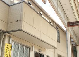 ベージュの外壁の２階建ての建物は商店街の一角にあり、２階部分にはベランダが付いている。