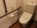 トイレの白い壁にはオレンジの呼び出しボタンとダークブランの手すりが設置されている。