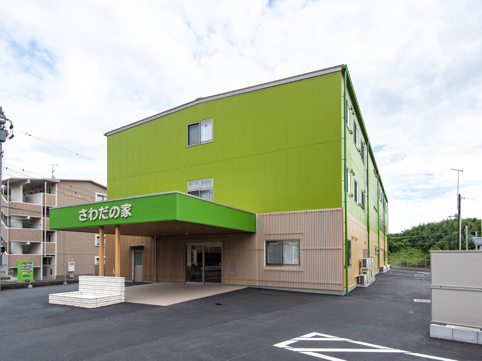 広い駐車場がある敷地内にはライトグリーンの3階建ての建物が建っている。玄関には車寄せが付いている。