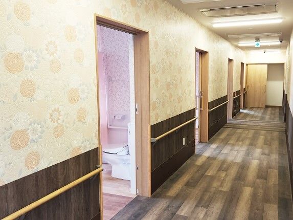 まっすぐな廊下。手すりと居室のドアが左側にあり、トイレも居室内にある。