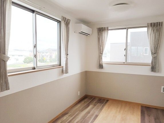 レースカーテンとカーテンがついた窓が二つ設置されたフローリングの部屋にはエアコンもある。