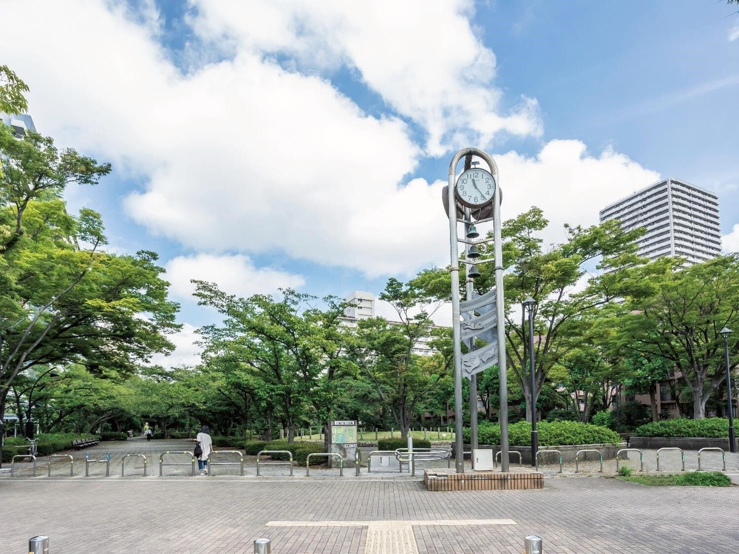 緑豊かな公園。大きな時計が中央の広場にあり、公園内を歩いている人の姿もある。