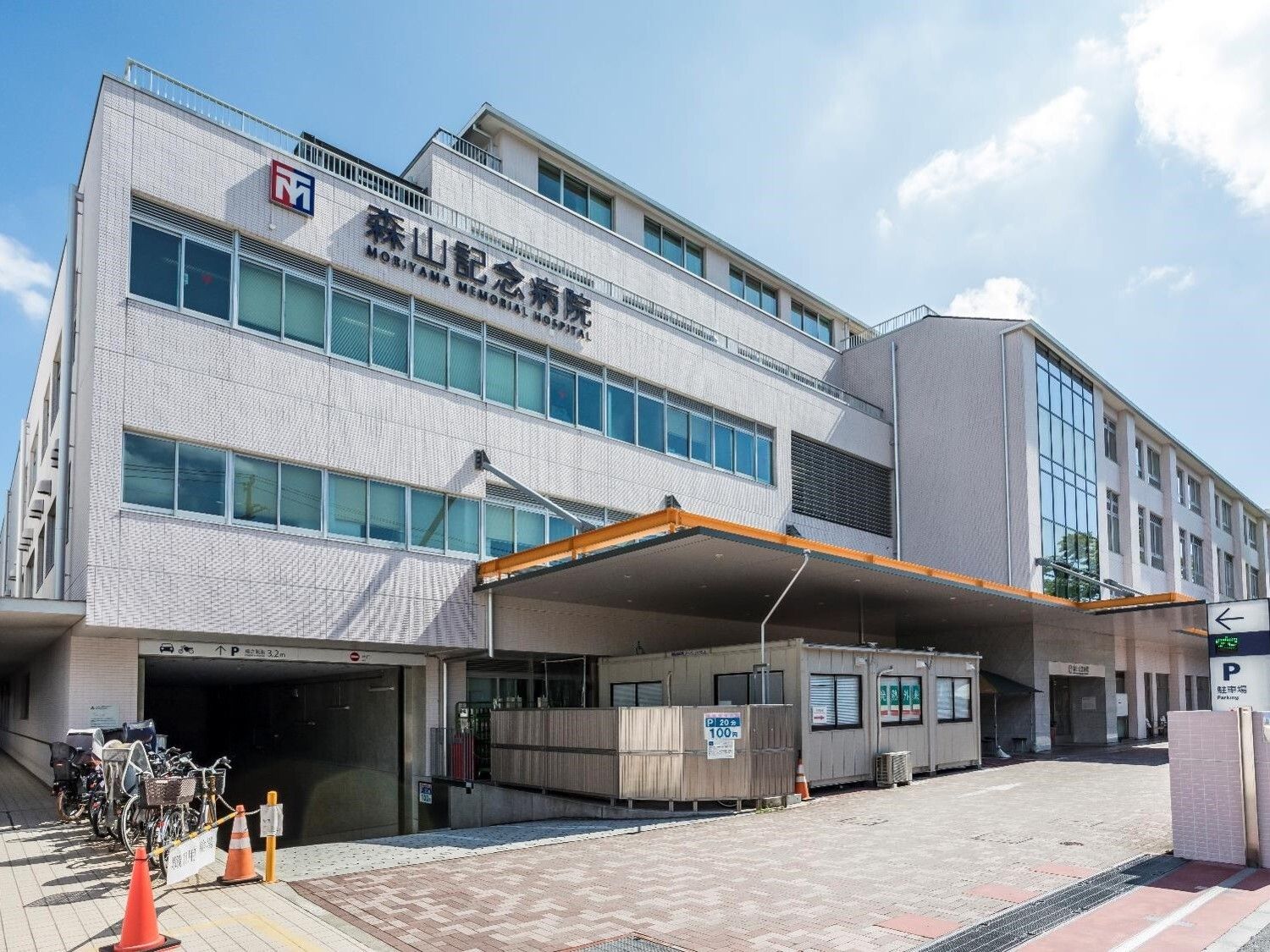 駐輪場に複数の自転車が止められた病院は大きく、日当たりのいい場所にあり、1階部分には屋根がある。