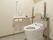 低い位置にオレンジの呼び出しボタンが付き、手すりや背もたれが付いたトイレが設置されている。