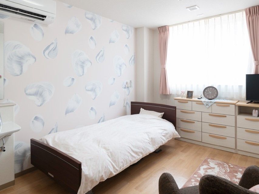 カーテン付きのフローリングの部屋。寝具付きベッドやタンス、エアコンなどがある。