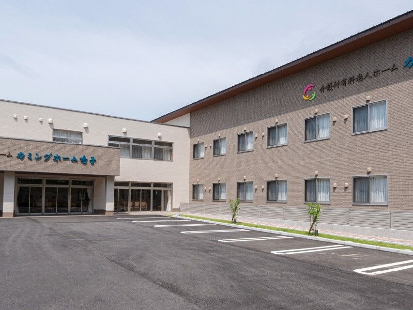 ベージュとブラウンの２階建ての建物はエル字型で日当たりのいい場所に建っている。敷地内には駐車場もある。