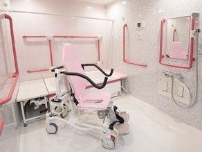 白を基調とした浴室にはたくさんの赤い手すりが付き、シャワーや浴室用車いすもある。
