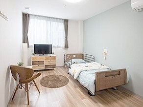 フローリングの部屋には寝具付きのベッドやテレビがあり、ベッドサイドには緊急通報装置がある。