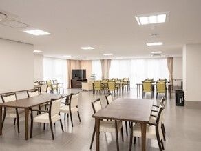 大きな窓が付いた食堂には木製のダイニングテーブルセットが複数置かれ、テレビもある。