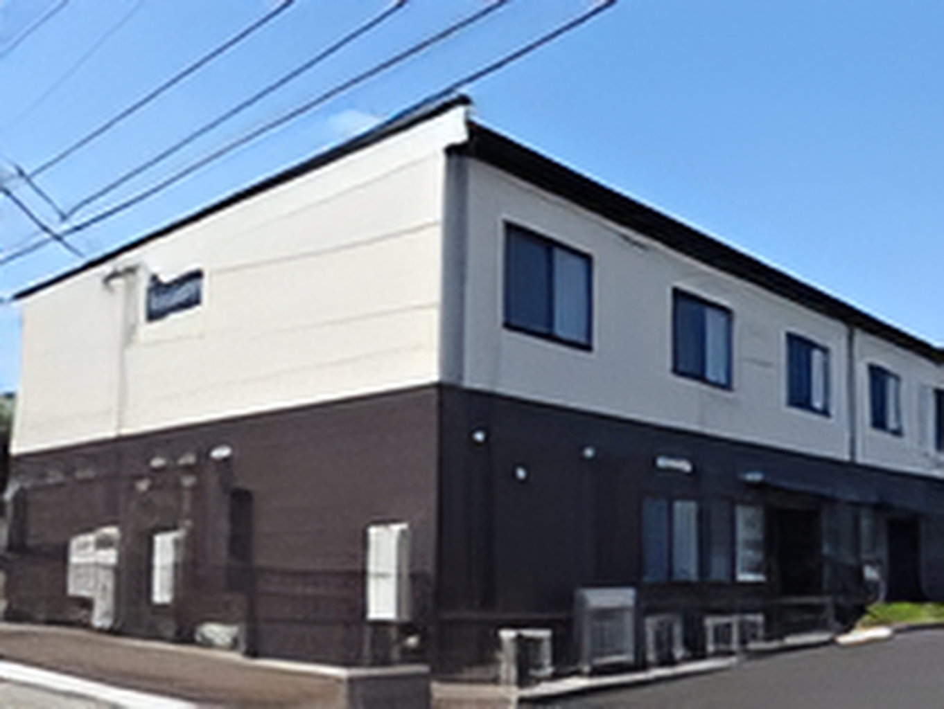白とダークグレーの２階建ての建物は日当たりのいい場所に建っていて、周りには背の高い建物はない。