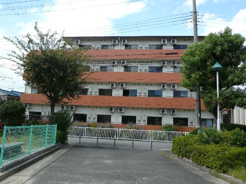 白を基調とした4階建ての建物の角フロアにベランダがあり、ベランダ部分はオレンジ。