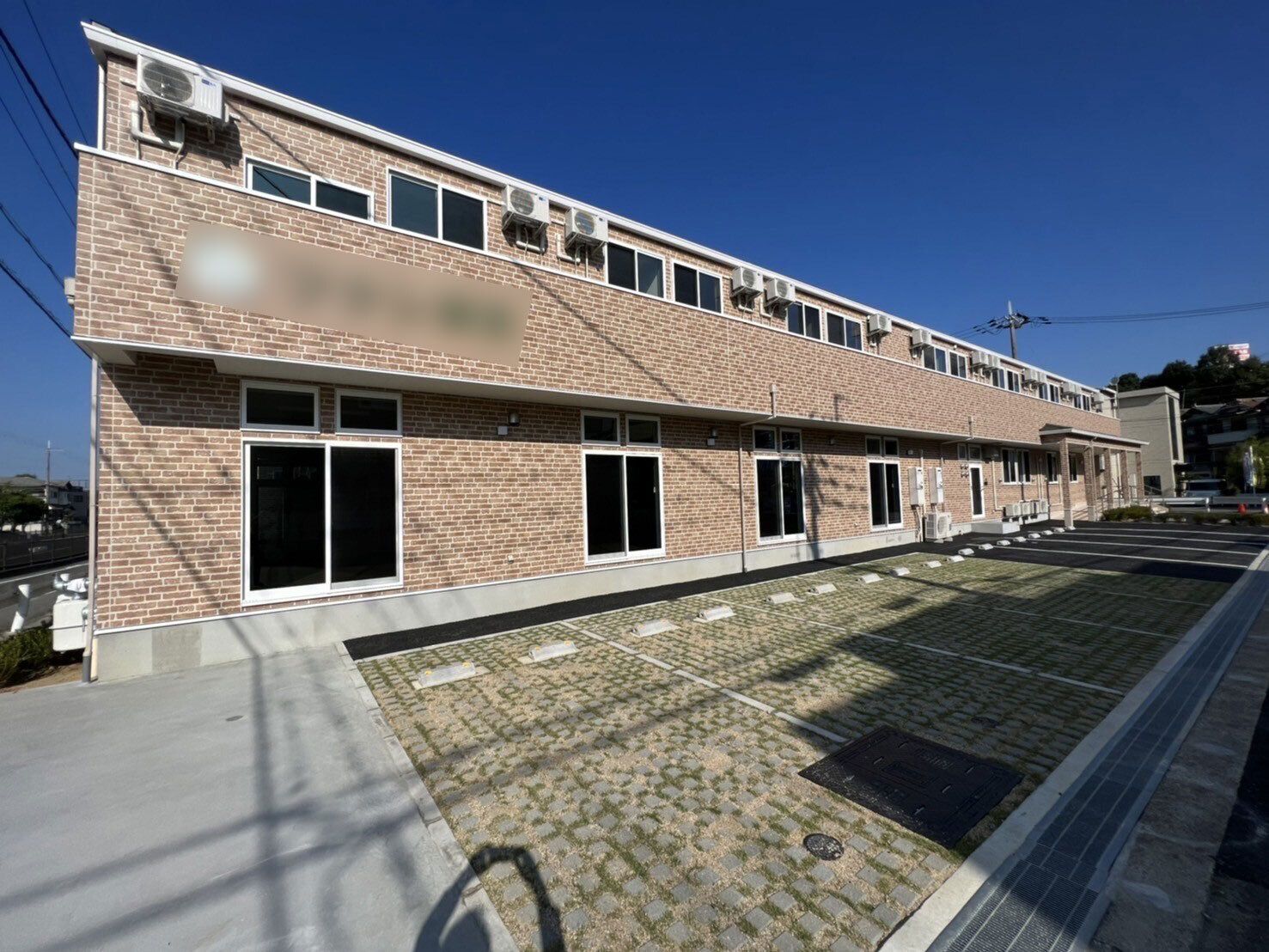 レンガ調の外壁の2階建ての建物は横に長く、建物の前には駐車場もある。