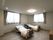 寝具付きのベッドが２台置かれたフローリングの部屋には大きな窓が付き、チェストも置かれている。