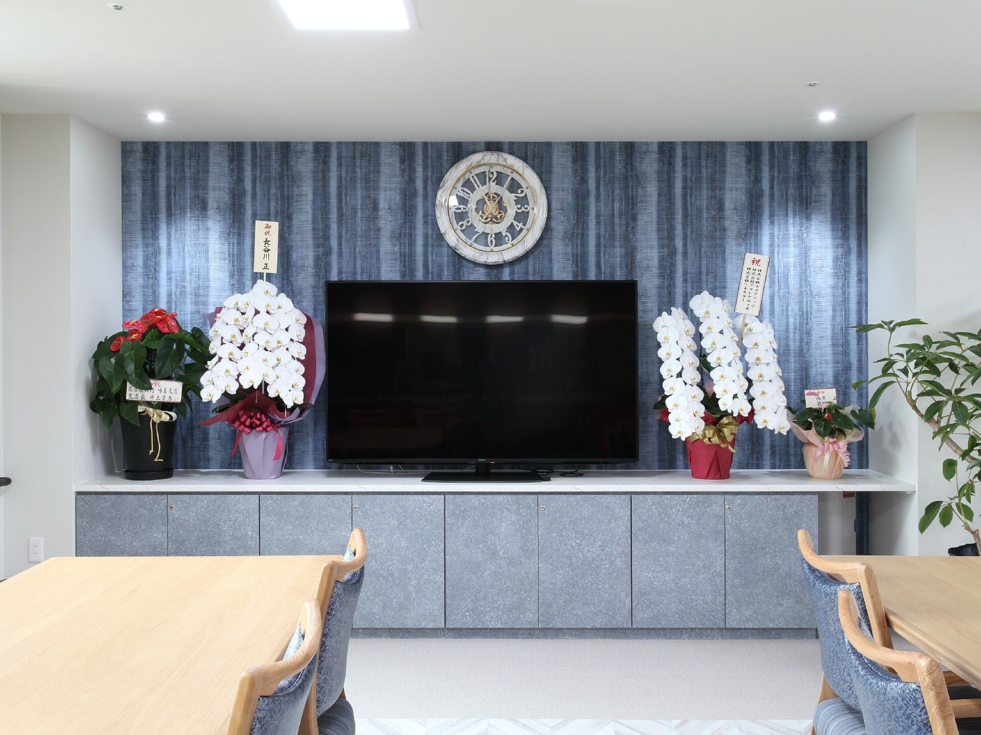 蘭の花がたくさん飾られた食堂には大きなテレビと複数のダイニングテーブルセットがある。