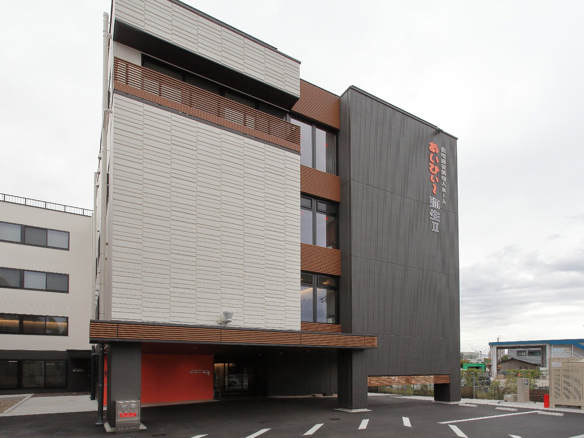 ベージュとダークグレーの外壁の大きな建物で、外壁にはホーム名が書かれている。広い駐車場もある。