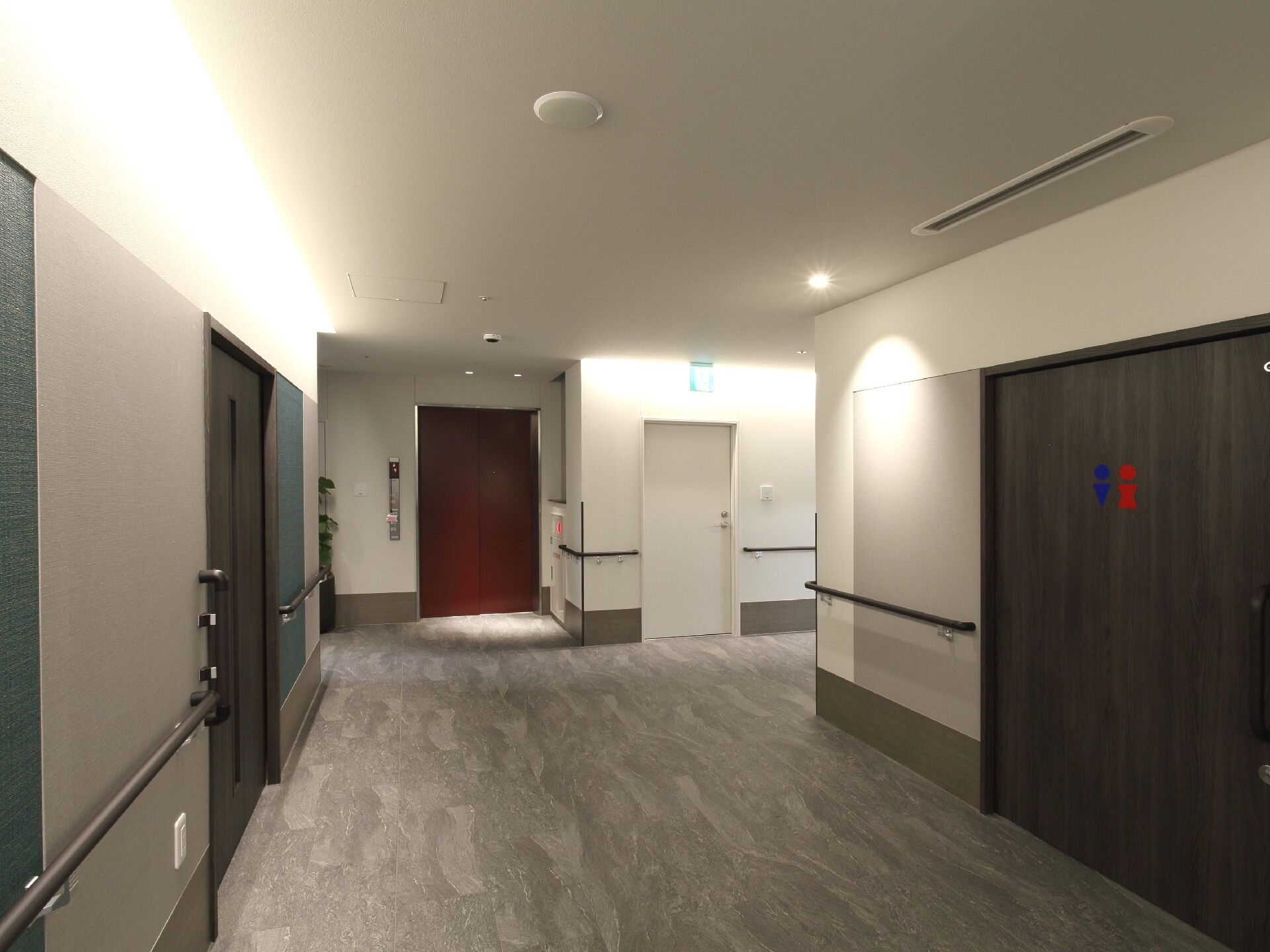 幅の広い廊下には手すりが付き、右側には男女のマークが書かれたトイレがあり、突き当りにはエレベーターもある。