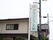 施設の入り口前に設置されている看板である。白い地にグリーンの文字で施設名が書かれ、一番上にはロゴマークがある。