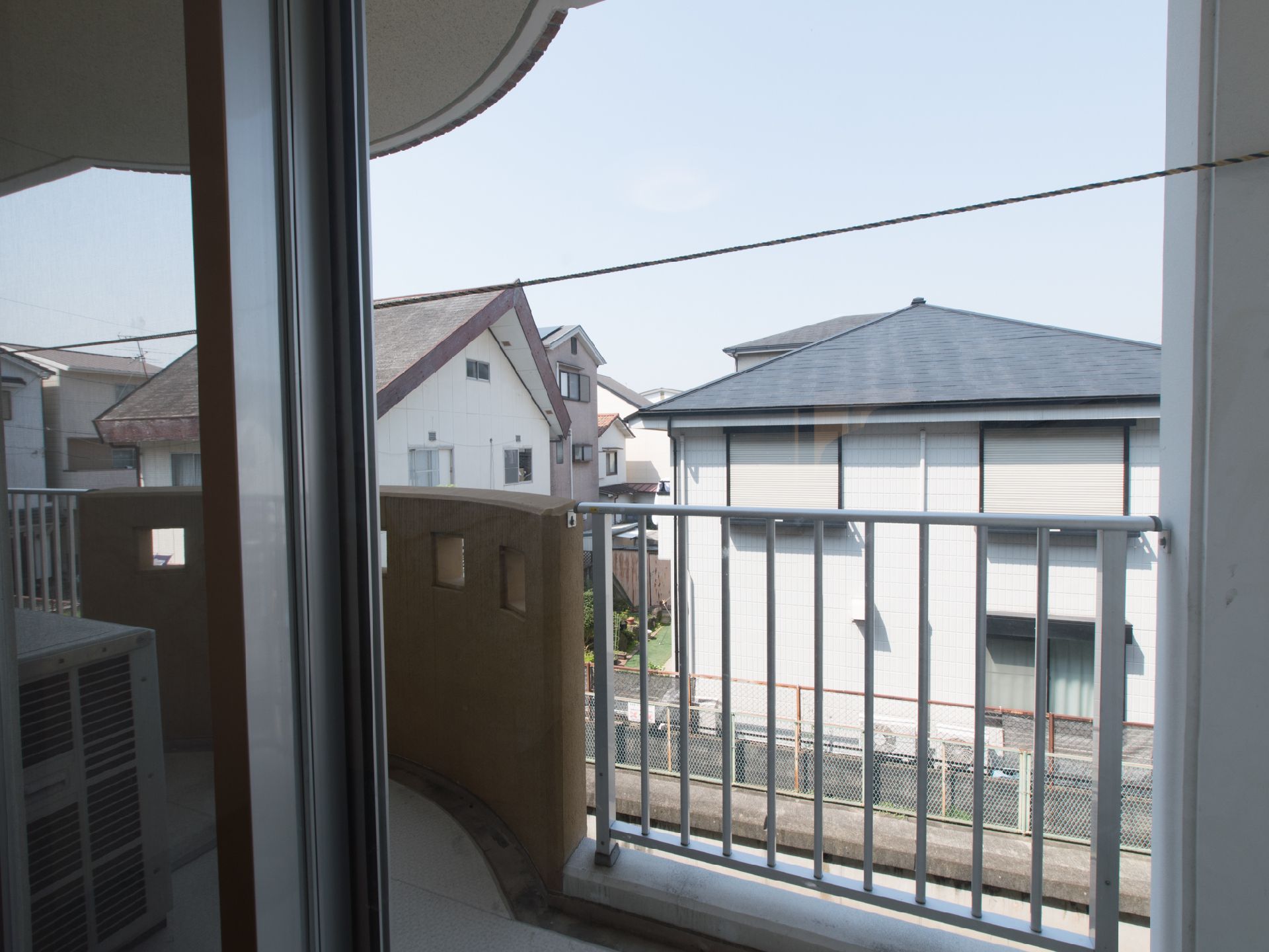 バルコニーは十分な高さの柵がついている。隣の部屋との境にも策が設置されている。窓の外は住宅街が広がっている。