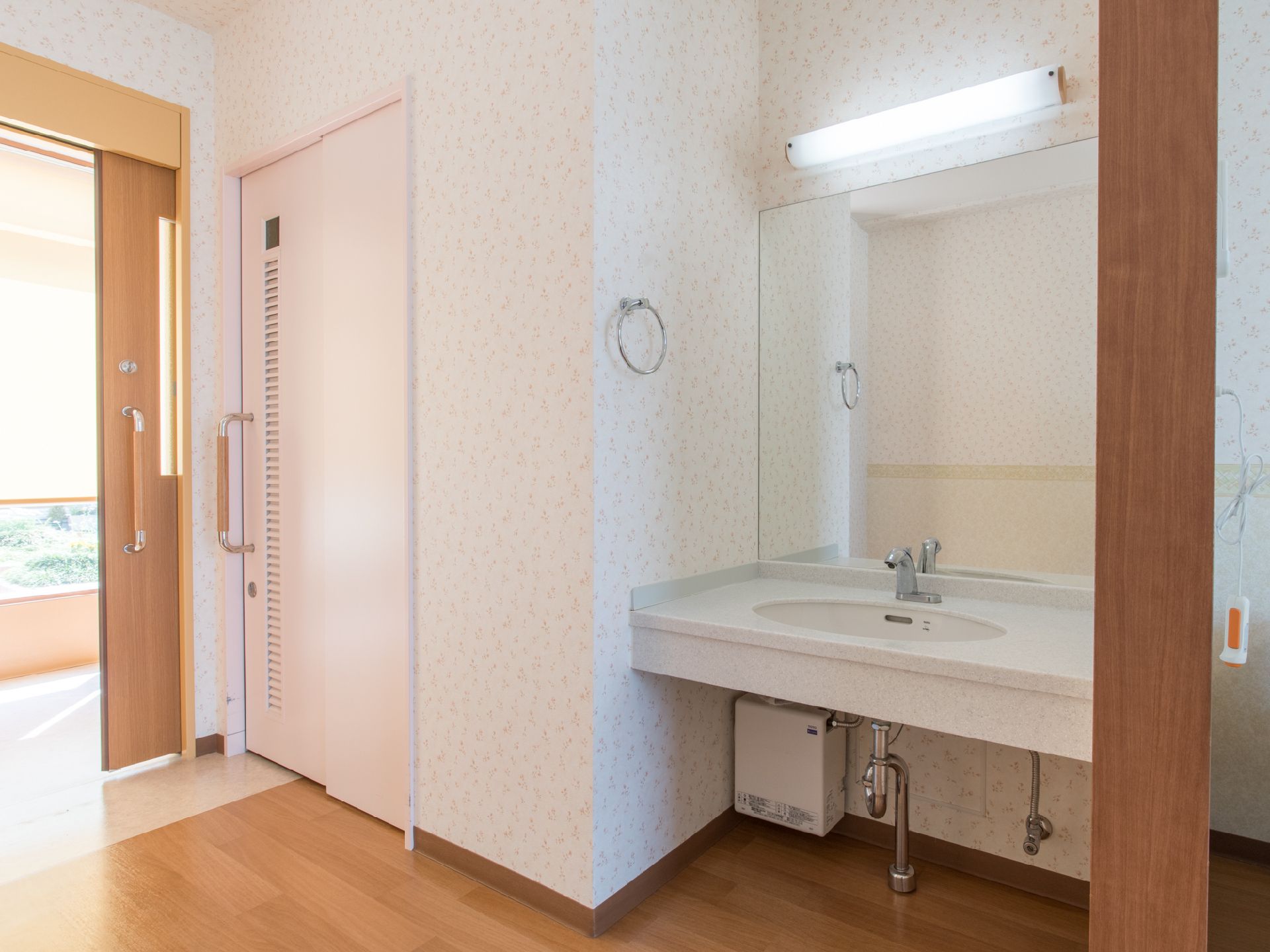 居室の入口付近にある、清潔感のある洗面台とトイレのドア