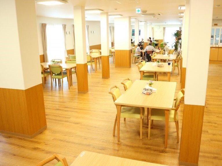 広々とした食堂にライトグリーンの椅子がセットされた木製のテーブルセットが多く並んでいる。