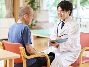 笑顔で高齢男性と話している白衣を着た男性スタッフ。2人は向かい合わせに座っている。