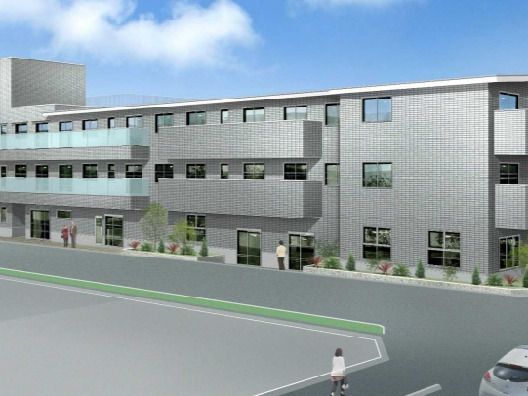 3階建てのグレーの建物の角フロアにベランダが付いていて、草木が周りに植えられている。