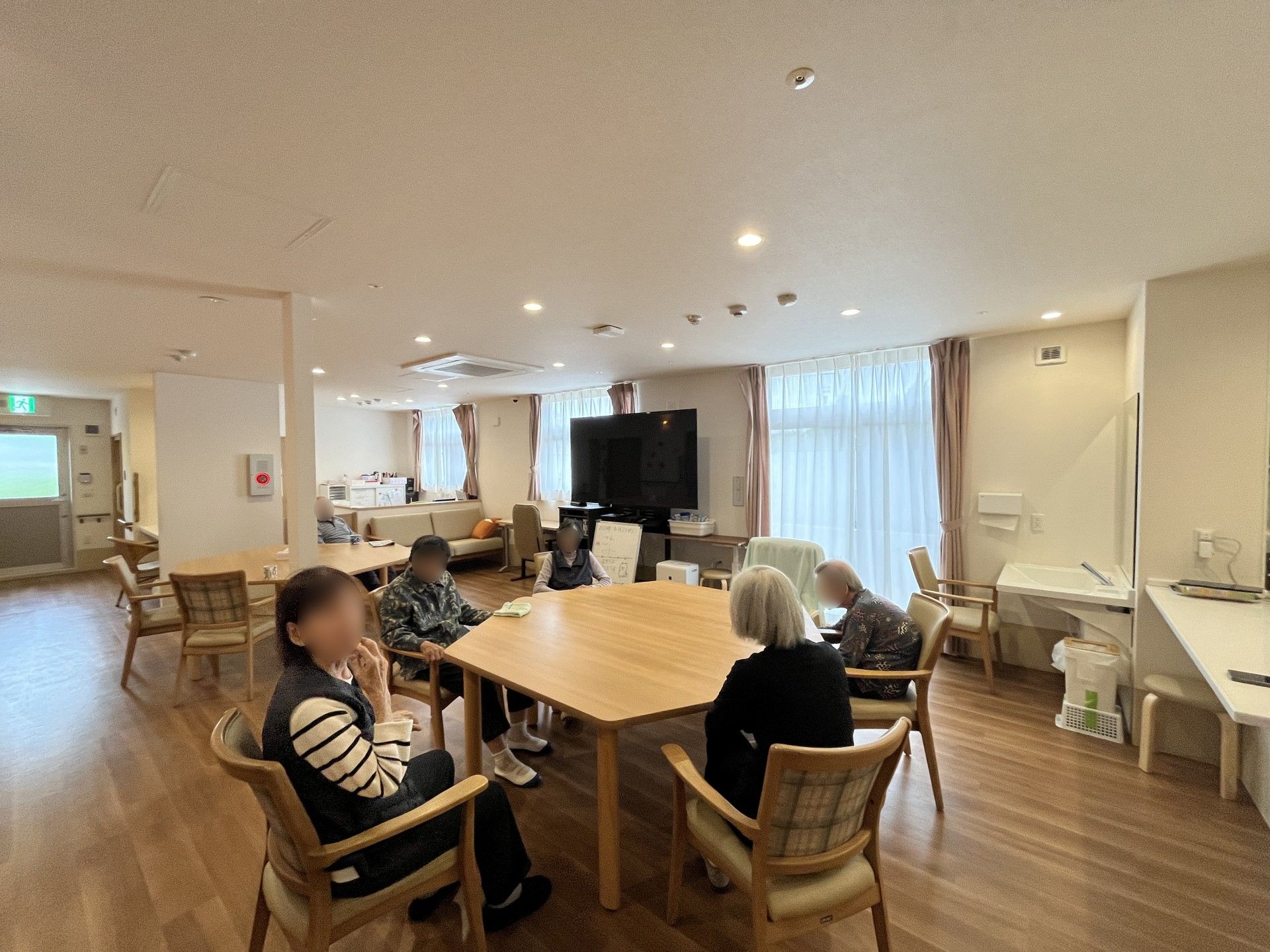 クリスマスの飾りつけがされた館内でサンタ帽をかぶってテーブルを囲む高齢者たち。スタッフはサンタの衣装を着ている。